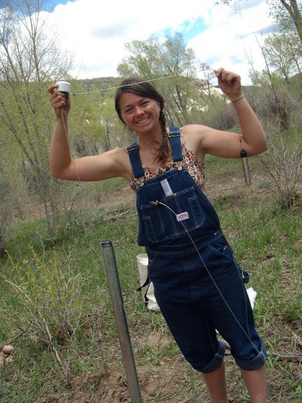 Dr. Melissa Clutter as a student in 2011, stands in overalls and holds tools to monitor groundwater.