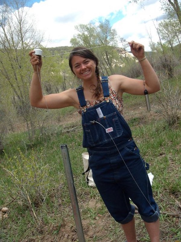 Dr. Melissa Clutter as a student in 2011, stands in overalls and holds tools to monitor groundwater